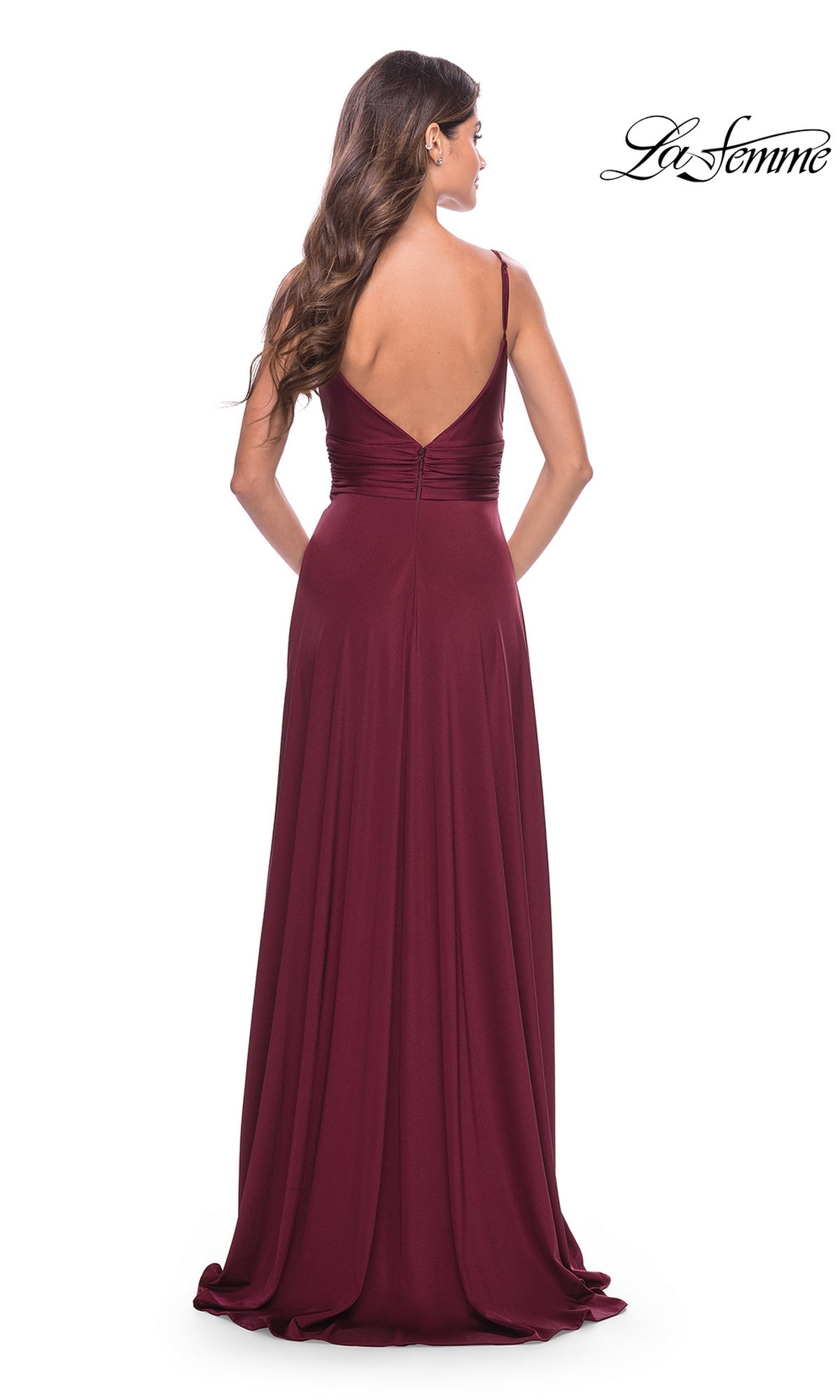 A woman wears the La Femme Simple Long A-Line Prom Dress 31090 in burgundy. The floor-length formal gown features thin straps and a deep V back as she poses with her back to the camera against a white background.